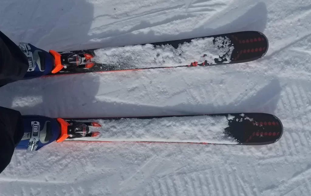 Deux skis Rossignol Experience 88 Ti chaussés sur une piste damée, vus d'en haut, de la neige sur le dessus des skis