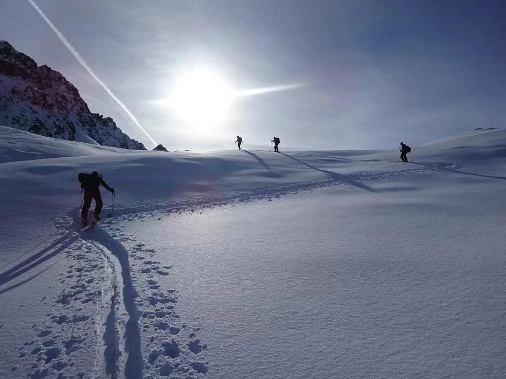 Quatre skieurs de randonnée en file sur un plateau enneigé, à contre-jour, au-dessus de Chamonix